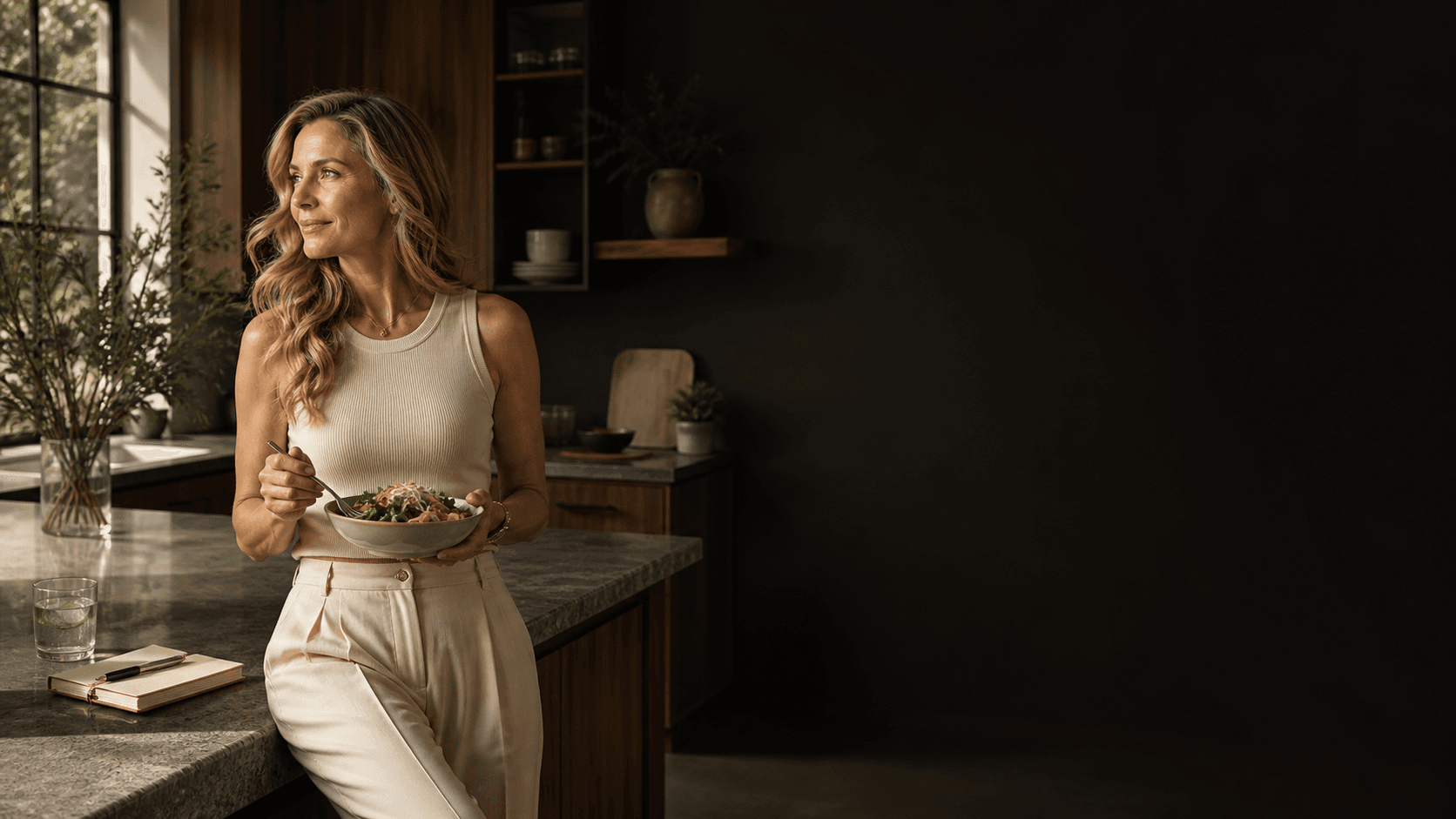 A woman holding a fresh salad in a warm modern kitchen